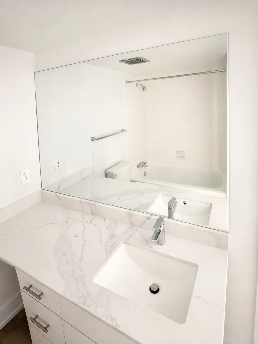 Wide frameless mirror across a white vanity wall