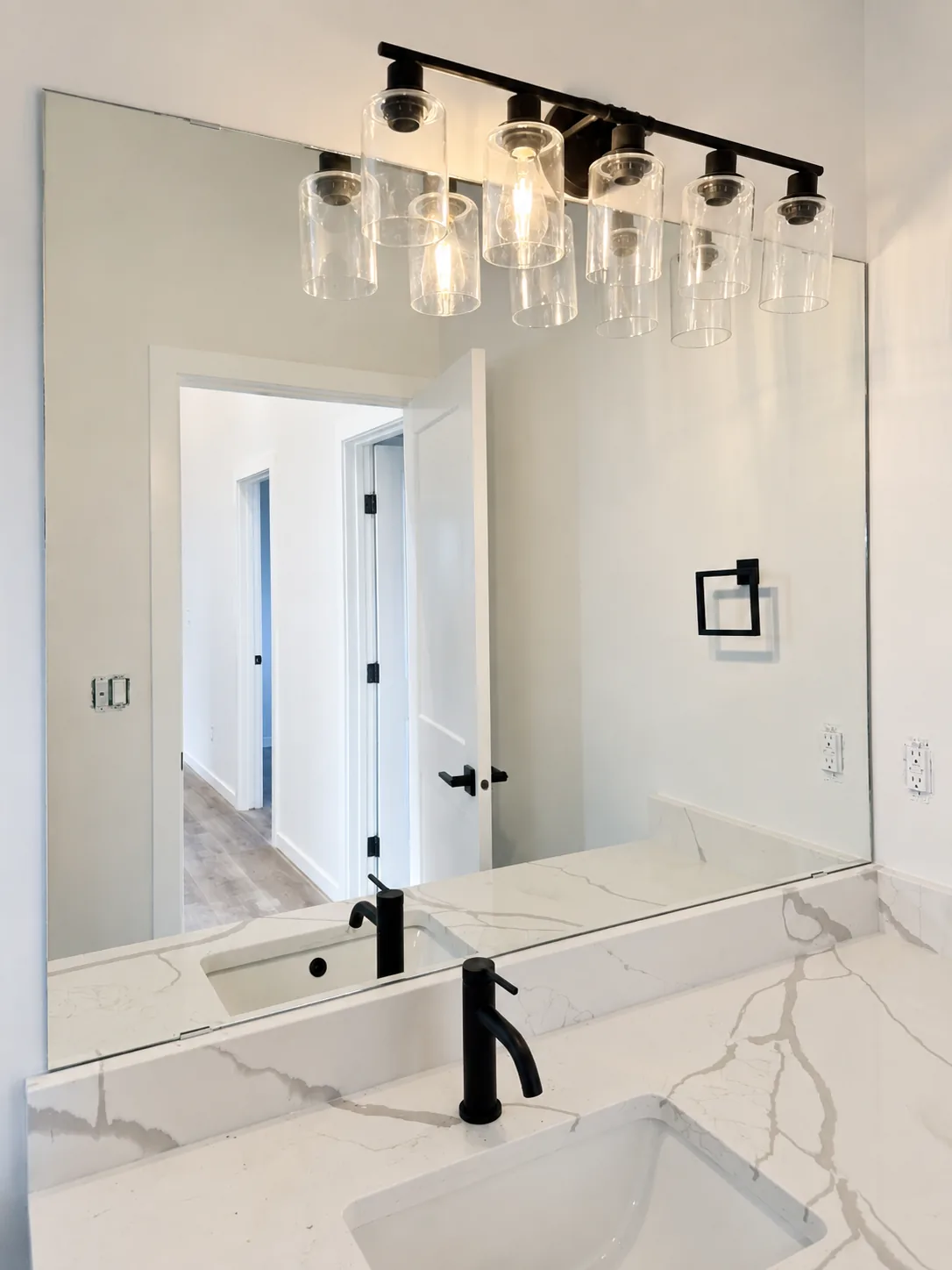 Large frameless vanity mirror over a marble counter with black fixtures
